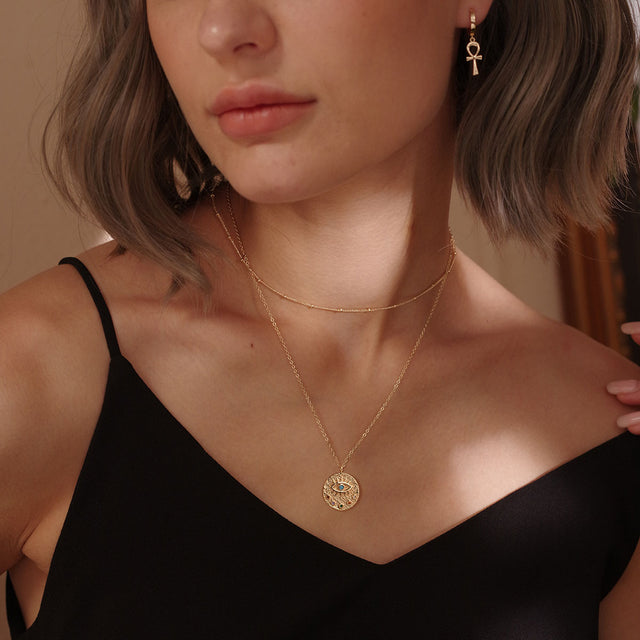 Model wearing Fettero® engraved evil eye gold pendant necklace for women, elegant everyday wear jewelry with protective symbolism